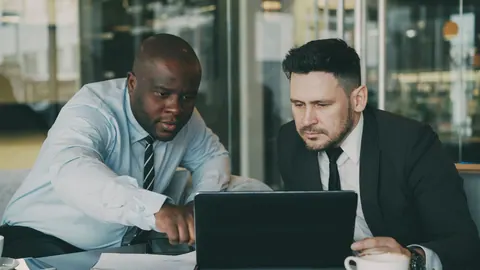 Dois executivos colaborando em um laptop, focados na tela.