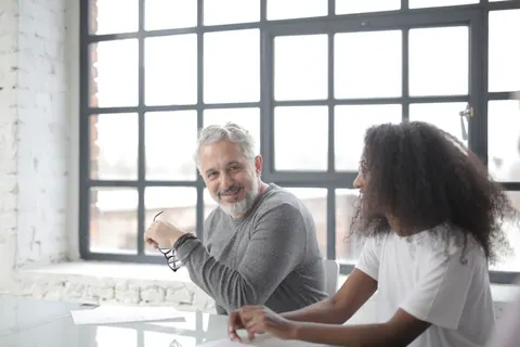 Mentor sênior e jovem estagiária negra sorrindo durante reunião de trabalho