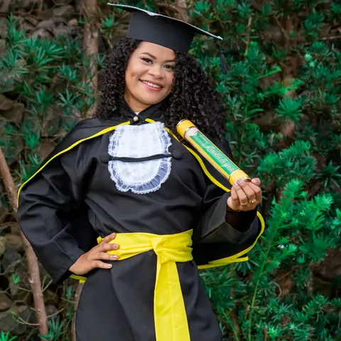 Mulher negra sorridente em beca de formatura segurando um diploma.
