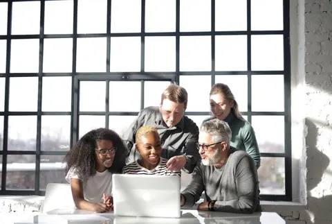 Grupo de colegas de trabalho diversos colaborando em laptop, promovendo aprendizado e desenvolvimento.