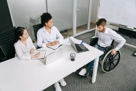Pessoas diversas em reunião de trabalho, incluindo homem em cadeira de rodas.