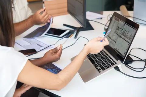 Pessoas analisando dados em um laptop, apontando para gráficos e informações.