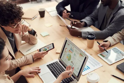 Pessoas em reunião de negócios analisando dados em laptop e tablet.