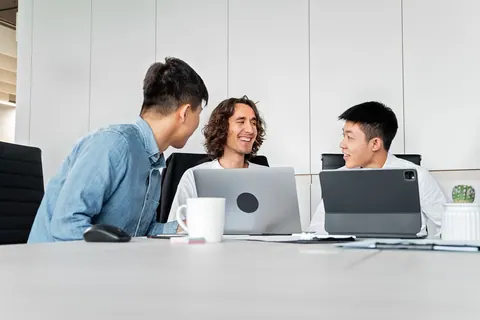 Pessoas em uma reunião de trabalho, conversando e usando laptops.