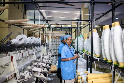 Mulher operando máquinas em uma fábrica têxtil, com carretéis de linha.