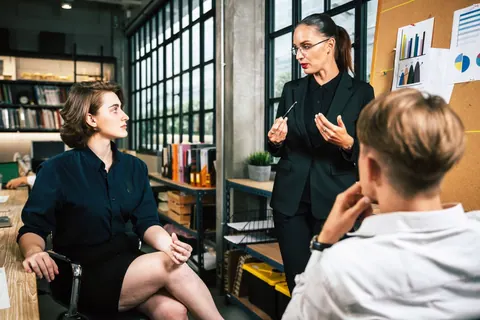 Líder feminina apresenta gráficos a dois colegas em reunião de escritório.