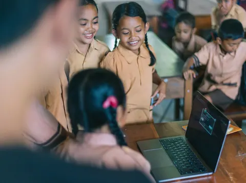 Crianças sorrindo enquanto observam um laptop com código de programação.
