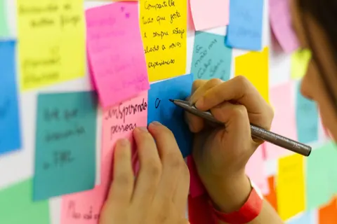 Pessoa escrevendo em post-its coloridos fixados em uma parede.