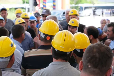 Grupo de trabalhadores com capacetes amarelos reunidos, representando a força de trabalho.