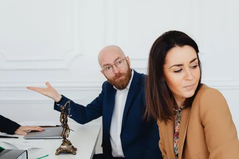 Homem irritado gesticula enquanto mulher ao lado desvia o olhar.