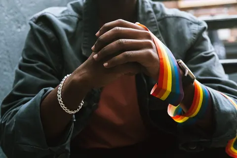 Mãos de um homem negro com uma pulseira de arco-íris, simbolizando a comunidade gay.