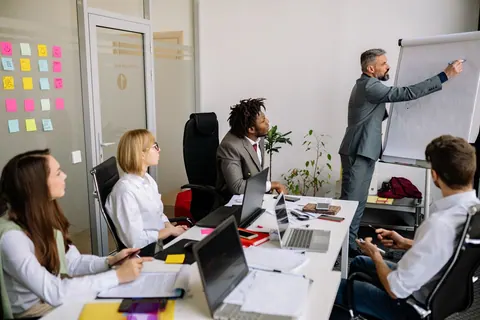 Homem apresentando em quadro branco para equipe em reunião de escritório.