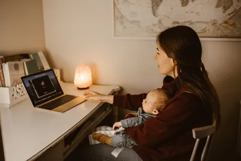 Mãe com bebê no colo em videochamada, conciliando maternidade e trabalho.