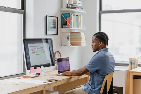 Homem trabalhando concentrado em seu computador e laptop em um escritório.