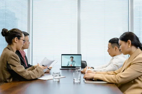 Profissionais em reunião híbrida com colega participando por videochamada.