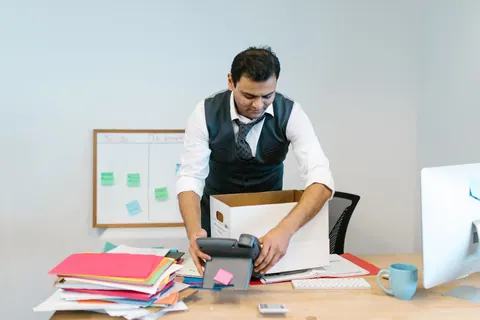 Homem de camisa e colete empacotando seus pertences em uma caixa no escritório.