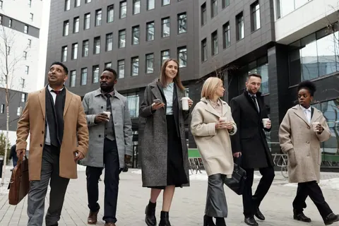 Seis colegas de trabalho de etnias diversas, vestindo casacos, caminham juntos na rua.