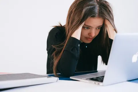 Mulher estressada olhando para um laptop, com as mãos na cabeça.