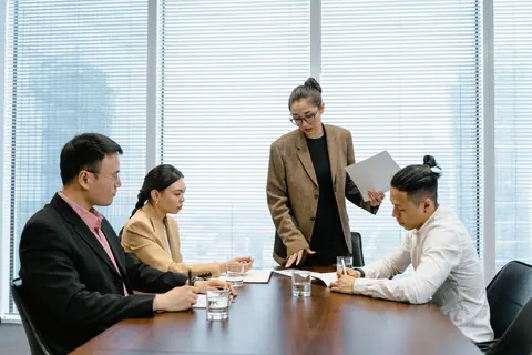 Colegas de trabalho discutindo em uma sala de reunião com janelas grandes.