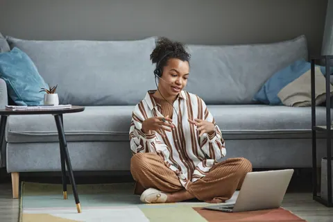 Mulher jovem sorrindo e gesticulando durante uma videochamada em seu laptop.