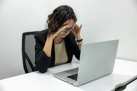 Jovem mulher estressada com as mãos na cabeça olhando para o laptop.