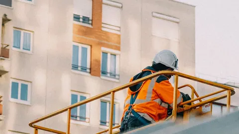 Trabalhador da construção civil em plataforma elevada, usando capacete e colete de segurança.