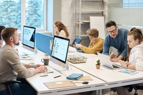 Pessoas trabalhando juntas em um escritório com computadores e laptops.