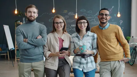 Equipe diversa e sorridente posa em escritório moderno com lousa e lâmpadas penduradas.