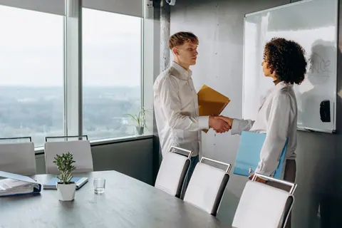 Dois colegas de trabalho se cumprimentando com um aperto de mãos em uma sala de reunião.