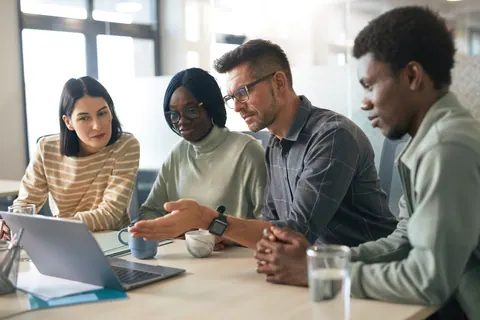 Grupo de profissionais diversos colaborando e aprendendo com um laptop.