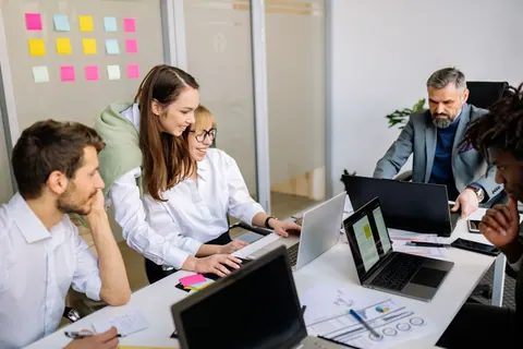 Colegas de trabalho colaborando em uma reunião de escritório, focados em laptops.
