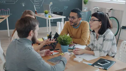 Equipe diversa colaborando em uma mesa de reunião com laptop e gráficos.