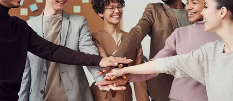 Pessoas de diversas etnias e gêneros com as mãos unidas em sinal de trabalho em equipe.