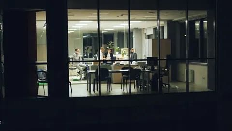Reunião de negócios em escritório moderno à noite, vista através da janela.