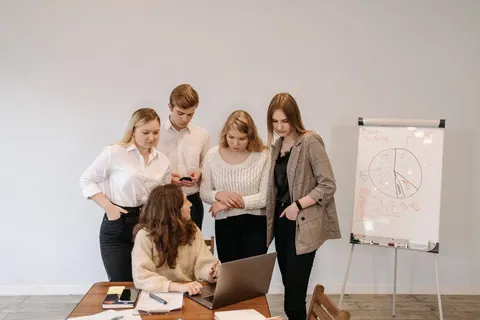 Equipe de RH colaborando em um projeto inovador com laptop e quadro branco.