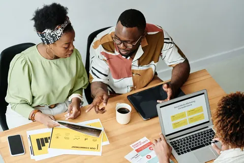 Pessoas em uma reunião de trabalho, olhando documentos e um laptop com gráficos.