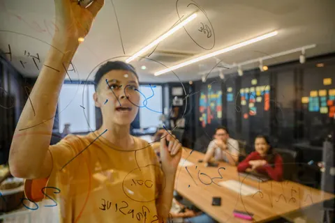 Pessoa escrevendo em quadro de vidro transparente durante reunião de negócios