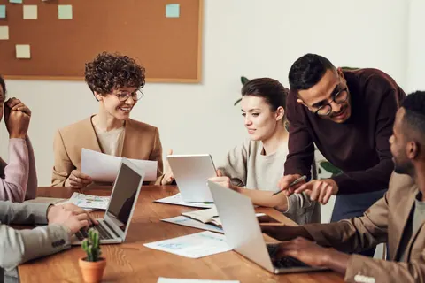 Pessoas diversas colaborando em uma mesa de reunião com laptops e documentos.