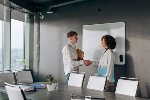 Pessoas de negócios apertando as mãos em uma sala de conferências, simbolizando parceria.