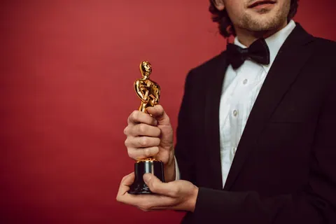 Homem de terno segurando um troféu dourado em frente a um fundo vermelho.