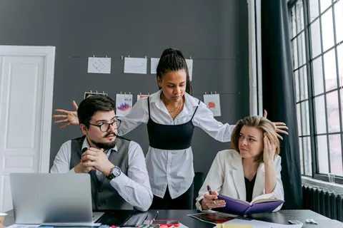 Três colegas de trabalho, um homem e duas mulheres, parecem confusos e frustrados.