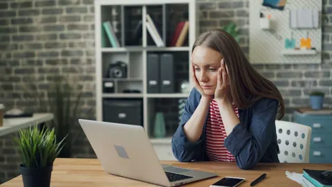 Mulher preocupada olhando para o computador em um escritório, com as mãos no rosto.