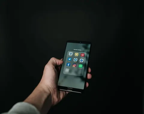Mão segurando um smartphone com a tela exibindo um grupo de ícones de aplicativos de redes sociais.
