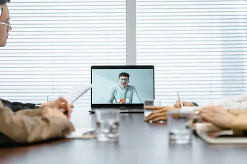 Pessoas em uma sala de reunião participando de uma entrevista virtual em um laptop.