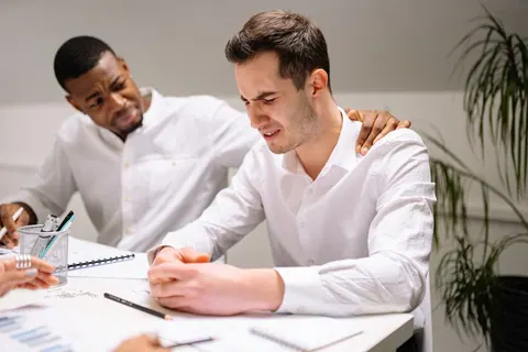 Homem consolando colega de trabalho estressado em ambiente de escritório.