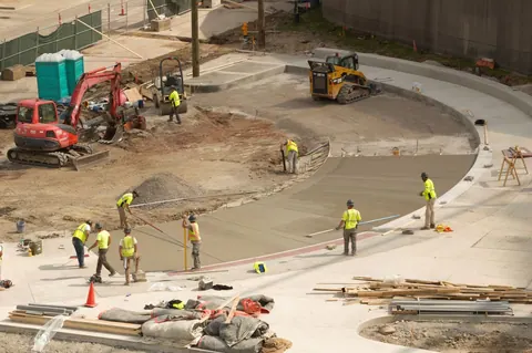 Trabalhadores da construção civil em um canteiro de obras, usando coletes de segurança.