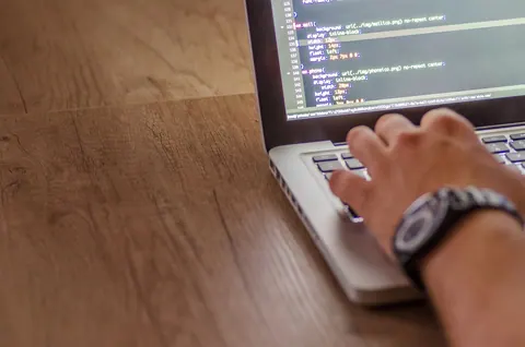 Mão de uma pessoa digitando em um notebook com código na tela.