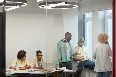Pessoas usando máscaras em um escritório moderno com paredes de vidro.