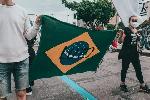 Pessoas segurando a bandeira do Brasil com uma máscara no centro.