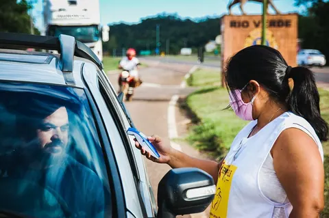 Mulher com máscara mede temperatura de motorista, refletindo impacto da pandemia.